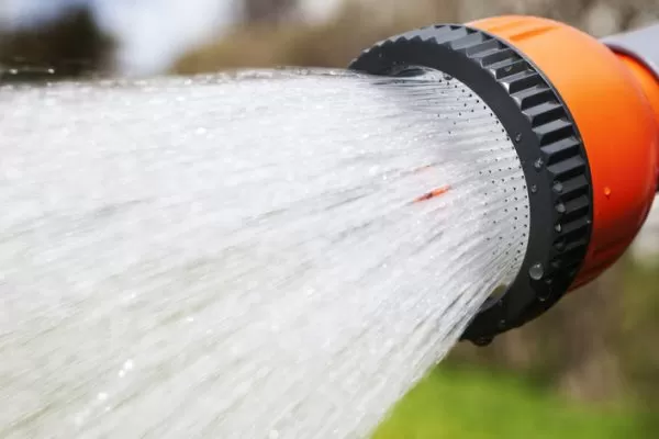 Hose spraying an artificial grass lawn for a deep clean